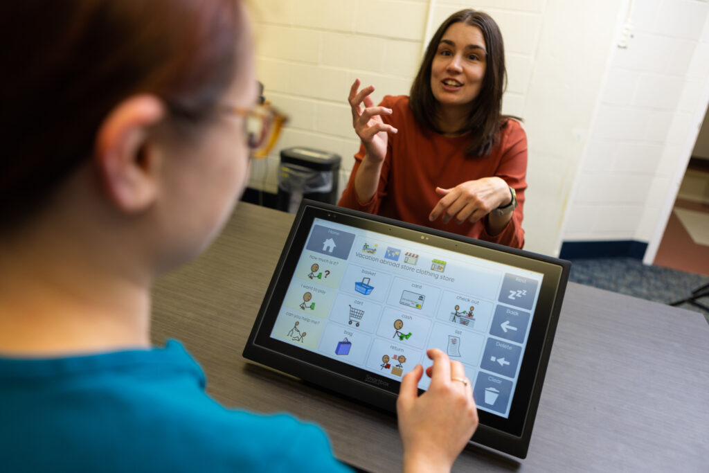 a student uses an AAC device while communicating with another student across a table