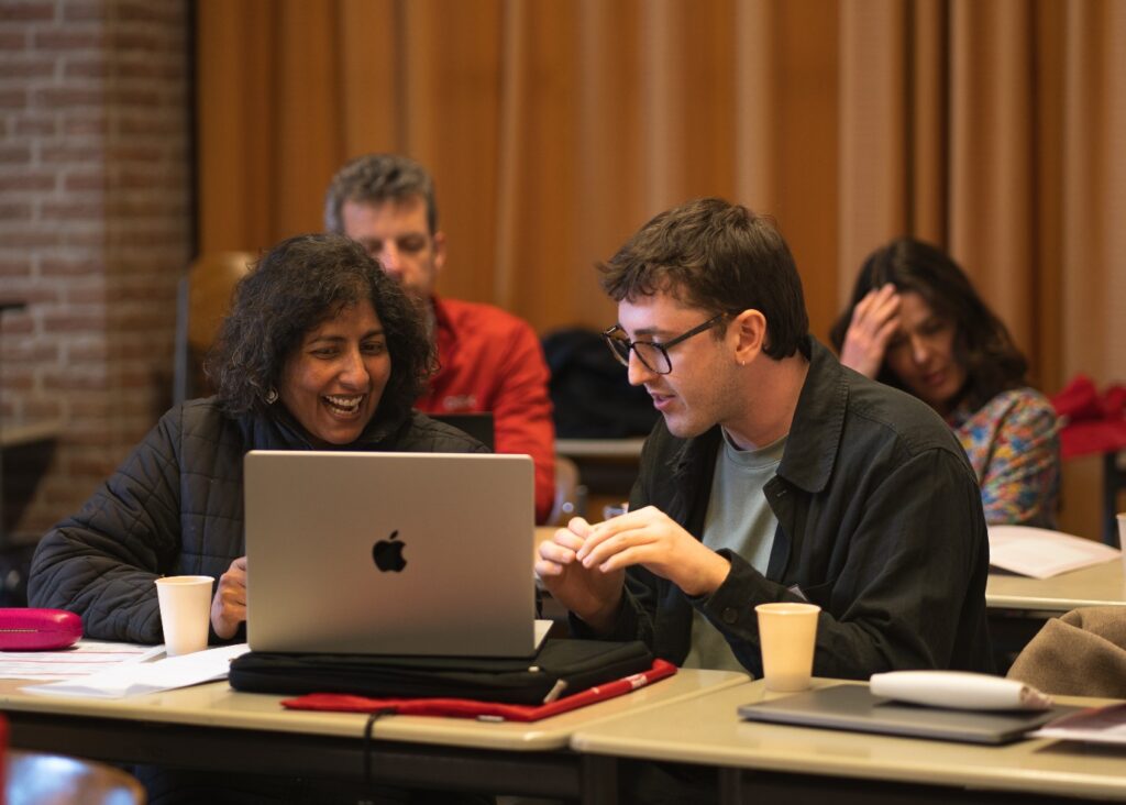 two conference attendees chat while looking at a shared laptop screen