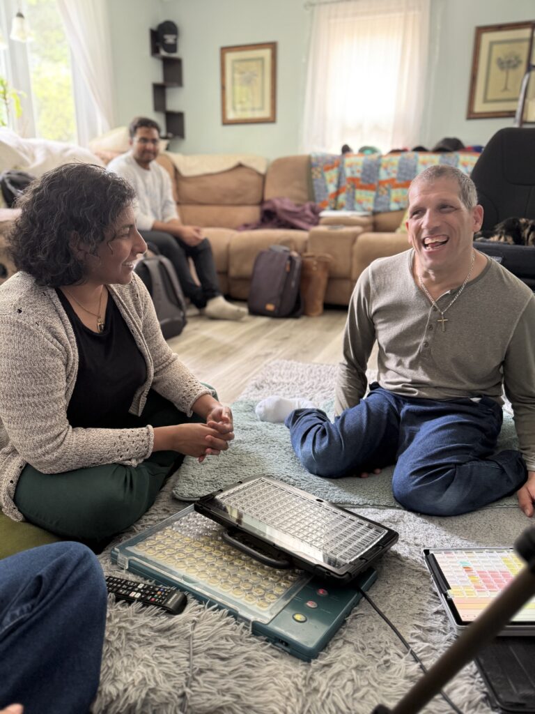 two people sitting on the floor having a conversation. One of them uses an AAC device to communicate