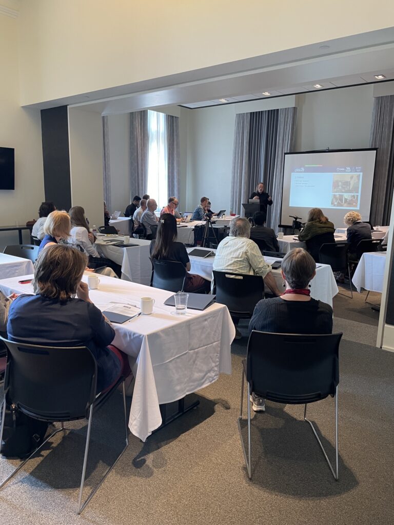 a group of workshop attendees sit in a conference room watching a powerpoint presentation